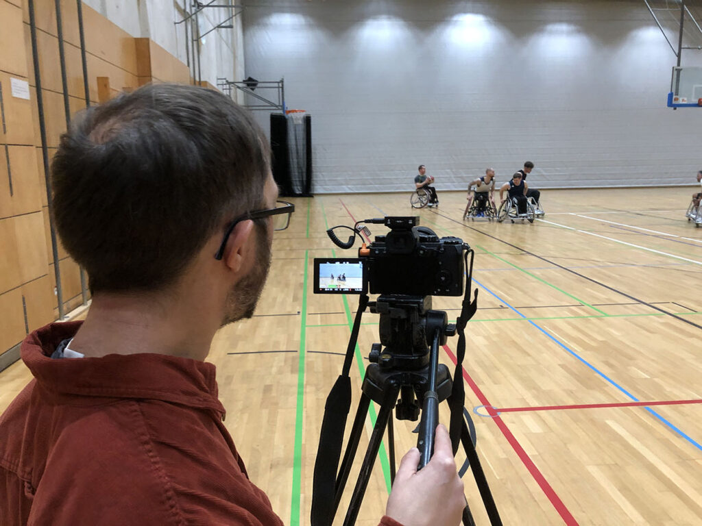 Ein Kameramann filmt Rollstuhlbasketballer in einer Sporthalle.