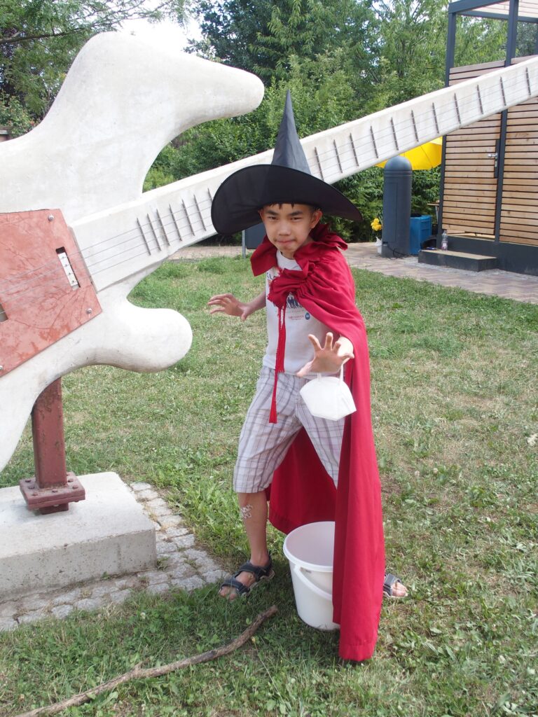 Ein Kind in Zaubererkostüm posiert neben der Skulptur einer großen Gitarre.