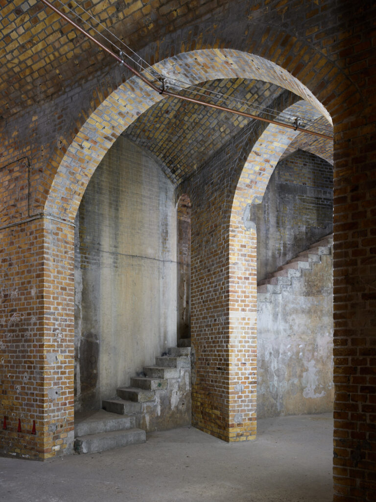 Mehrere Torbögen bilden eine Flucht. Rechts führt eine offene Treppe nach oben.