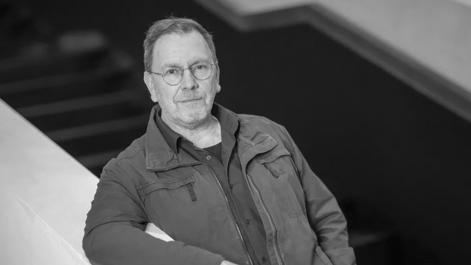 Schwarz/weiß-Bild von René Pollesch auf einer Treppe stehend. den Arm auf der Brüstung gelehnt.